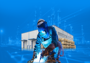 Industrial welder working in a heavy engineering manufacturing facility with fabrication unit, warehouse infrastructure, and industrial plant in the background.